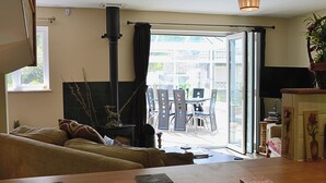 A cozy living room with a fireplace, a dining area with chairs and a table, and a view through a glass door to the outside. - 4 bedroom accommodation in Dunster, near Minehead (Dunster, near Minehead)