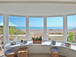 A bay window with a view of a pebbled beach and the sea.