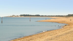 A beach with a clear sky, calm water, and a distant shoreline with vegetation. - 4 bedroom accommodation in Pagham, near Chichester (Pagham, near Chichester)