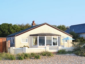 Ein eingeschossiges Haus mit geneigtem Dach, Schornstein und einem großen Fenster mit Blick auf den Garten.