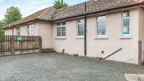A building with a gravel driveway, a wooden fence, and a green sign. - 2 bedroom accommodation in Meathop, near Grange-over-Sands (Meathop, near Grange-over-Sands)