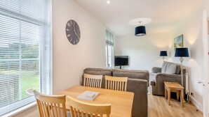 A modern living room with a dining table, two sofas, a TV, and a clock on the wall. - 2 bedroom accommodation in Meathop, near Grange-over-Sands (Meathop, near Grange-over-Sands)