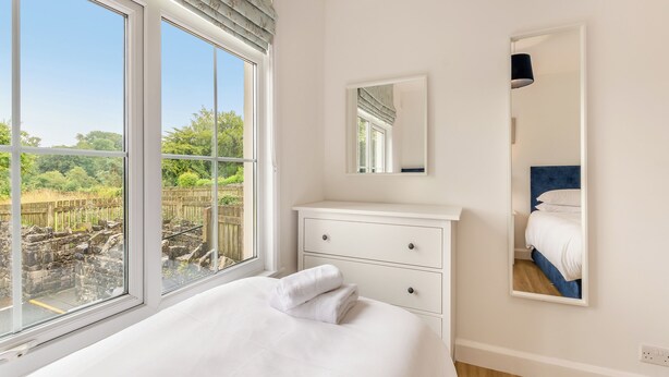 A bedroom with a large window, a bed with white bedding, a white dresser, and a mirror. - 2 bedroom accommodation in Meathop, near Grange-over-Sands (Meathop, near Grange-over-Sands)