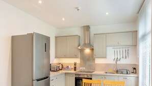 A compact kitchen with a refrigerator, stove, and dining area with chairs and a table. - 2 bedroom accommodation in Meathop, near Grange-over-Sands (Meathop, near Grange-over-Sands)