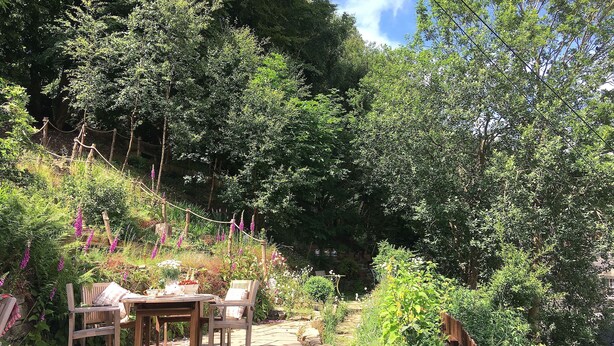 A garden patio with a table and chairs, surrounded by lush greenery and flowering plants. - 3 bedroom accommodation in Hebden Bridge Birkenhead Cottage (Hebden Bridge Birkenhead Cottage)