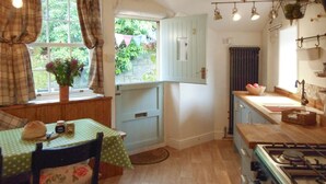 A small kitchen with a dining table, a stove, and a window with curtains. - 3 bedroom accommodation in Hebden Bridge Birkenhead Cottage (Hebden Bridge Birkenhead Cottage)