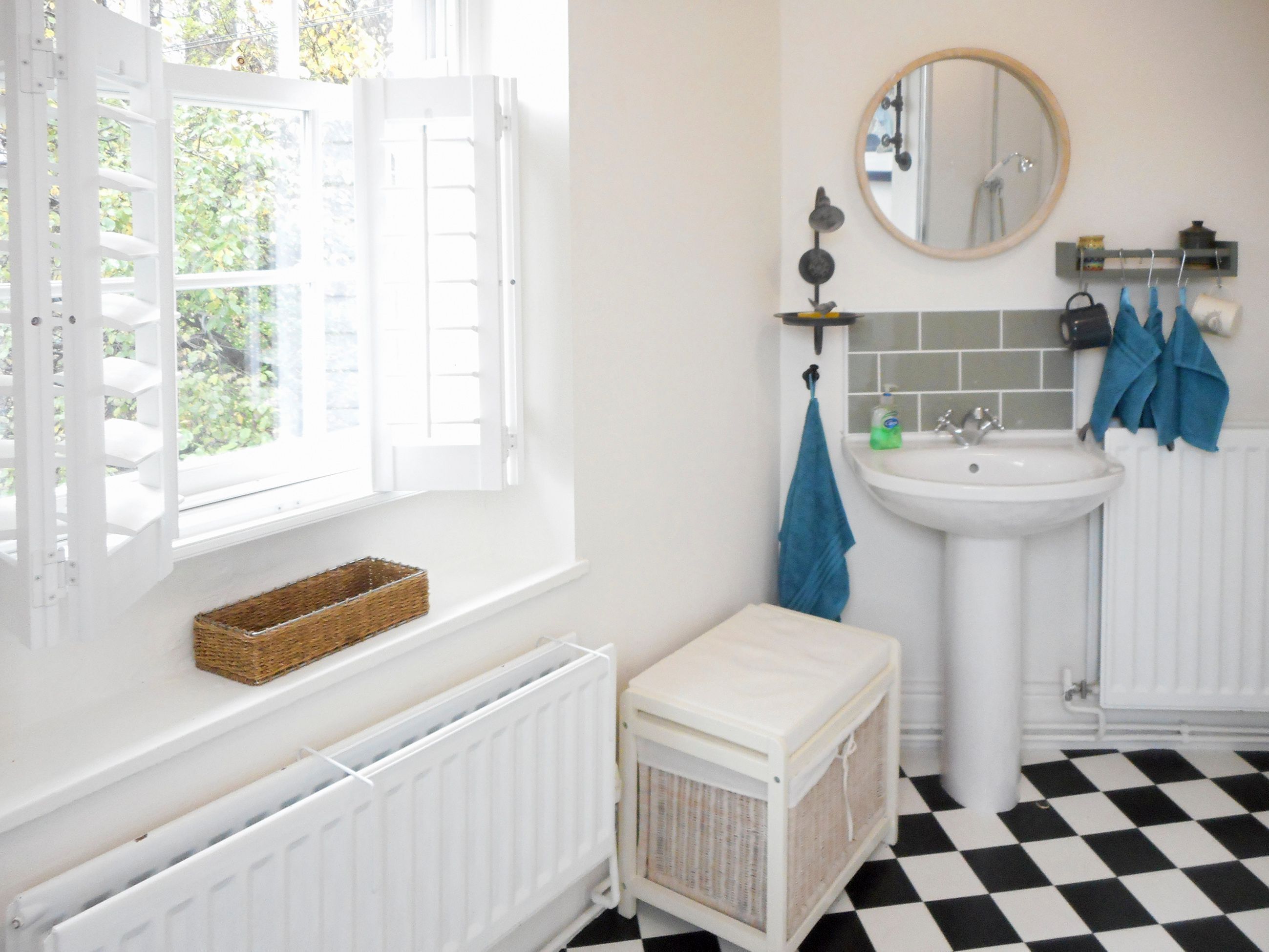 Ein Badezimmer mit weißem Heizkörper, Waschbecken, Spiegel und einem schwarz-weißen Schachbrettfußboden.