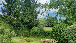 A garden with a wooden table and chairs, surrounded by lush greenery and trees.