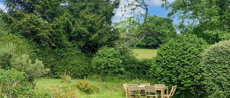A garden with a wooden table and chairs, surrounded by lush greenery and trees.