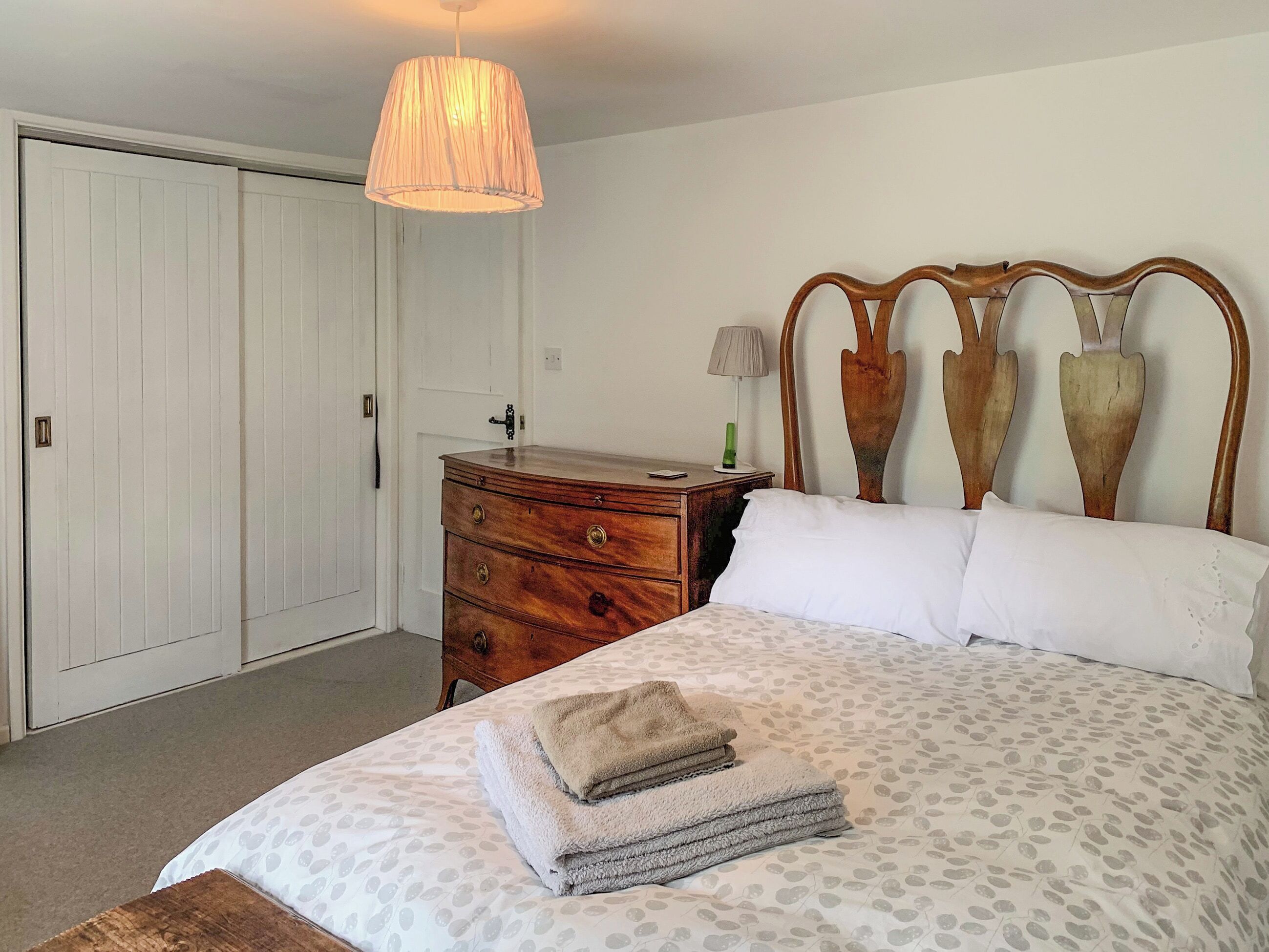 A bedroom with a bed, a wooden dresser, a nightstand, a lamp, and a hanging light fixture.