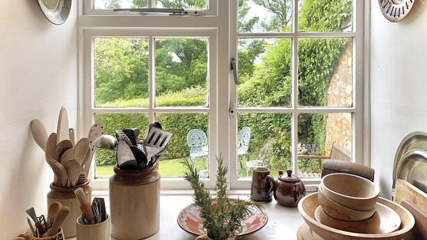 A kitchen with wooden utensils, a teapot, and a view of a garden through a large window.