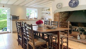 A dining area with a wooden table and chairs, a fireplace, and a kitchen in the background.