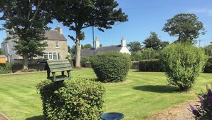 A well-maintained garden with a stone bench, a birdbath, and neatly trimmed hedges. - 1 bedroom accommodation in Castletown, near Thurso (Castletown, near Thurso)