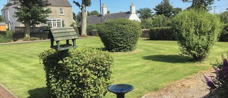 A well-maintained garden with a stone bench, a birdbath, and neatly trimmed hedges.