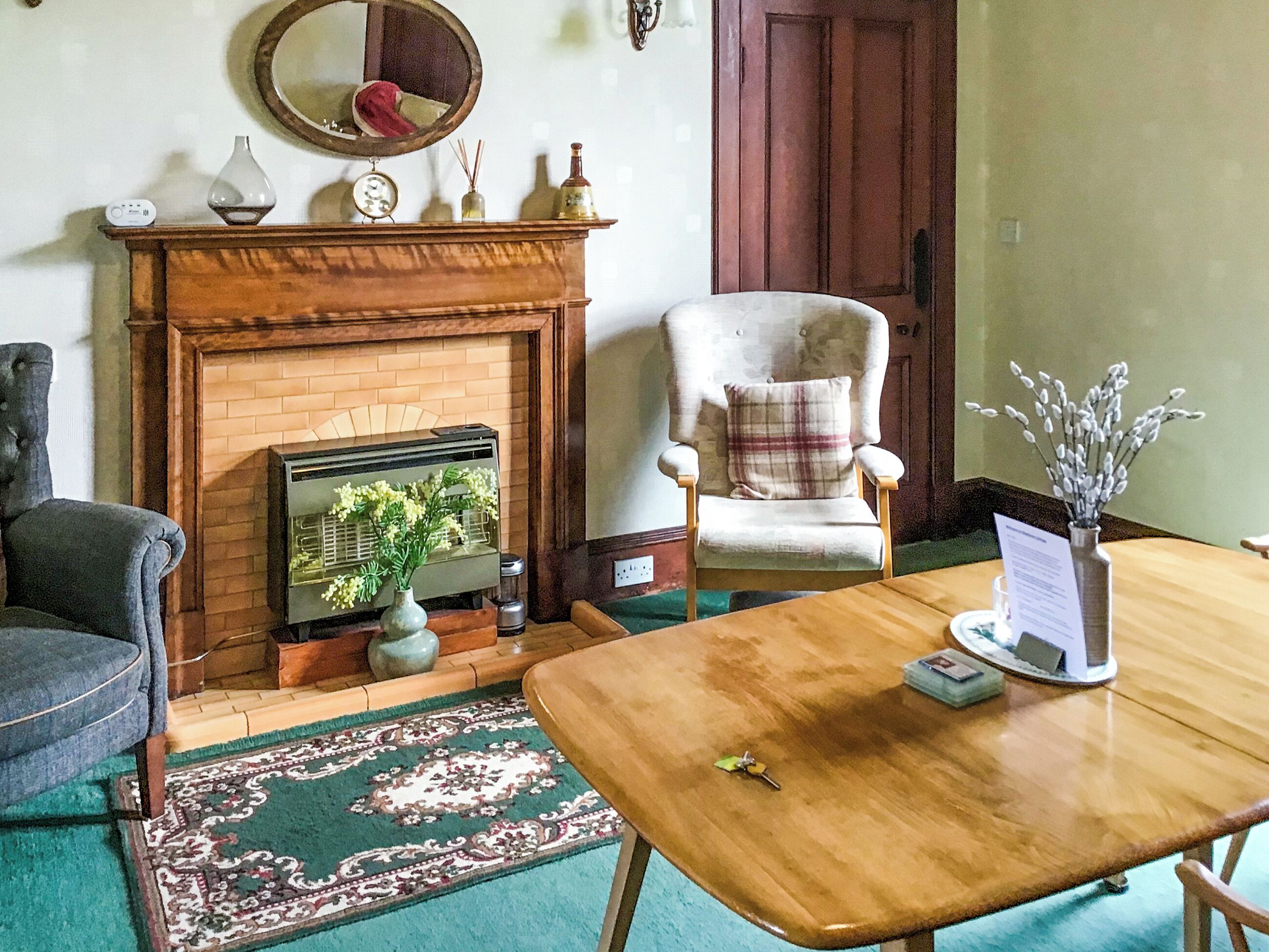 Une pièce avec une cheminée, un fauteuil, une table et un tapis.