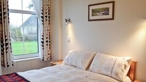 A bedroom with a bed, a nightstand, a window with curtains, and a framed picture on the wall. - 1 bedroom accommodation in Castletown, near Thurso (Castletown, near Thurso)