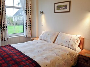 A bedroom with a bed, a nightstand, a window with curtains, and a framed picture on the wall. - 1 bedroom accommodation in Castletown, near Thurso (Castletown, near Thurso)