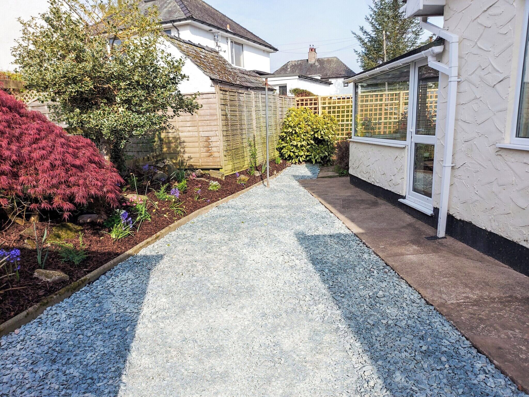 A garden pathway leading to a house with a white exterior and a window with a white frame.