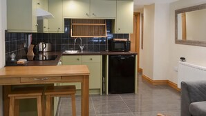 Een kleine keuken met groene kastjes, een zwart aanrecht, een spoelbak, een magnetron en een vaatwasser.