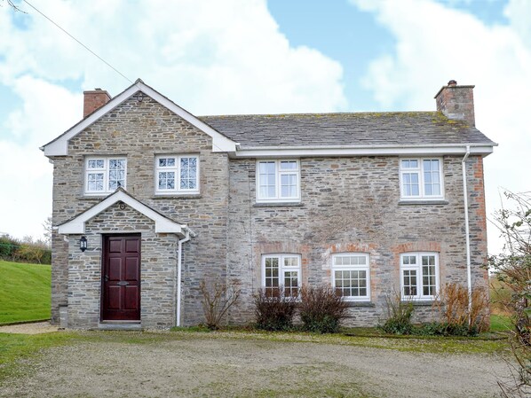 A two-story stone house with a red door, multiple windows, and a gravel driveway. - 4 bedroom accommodation in Edmonton, near Wadebridge (Edmonton, near Wadebridge)