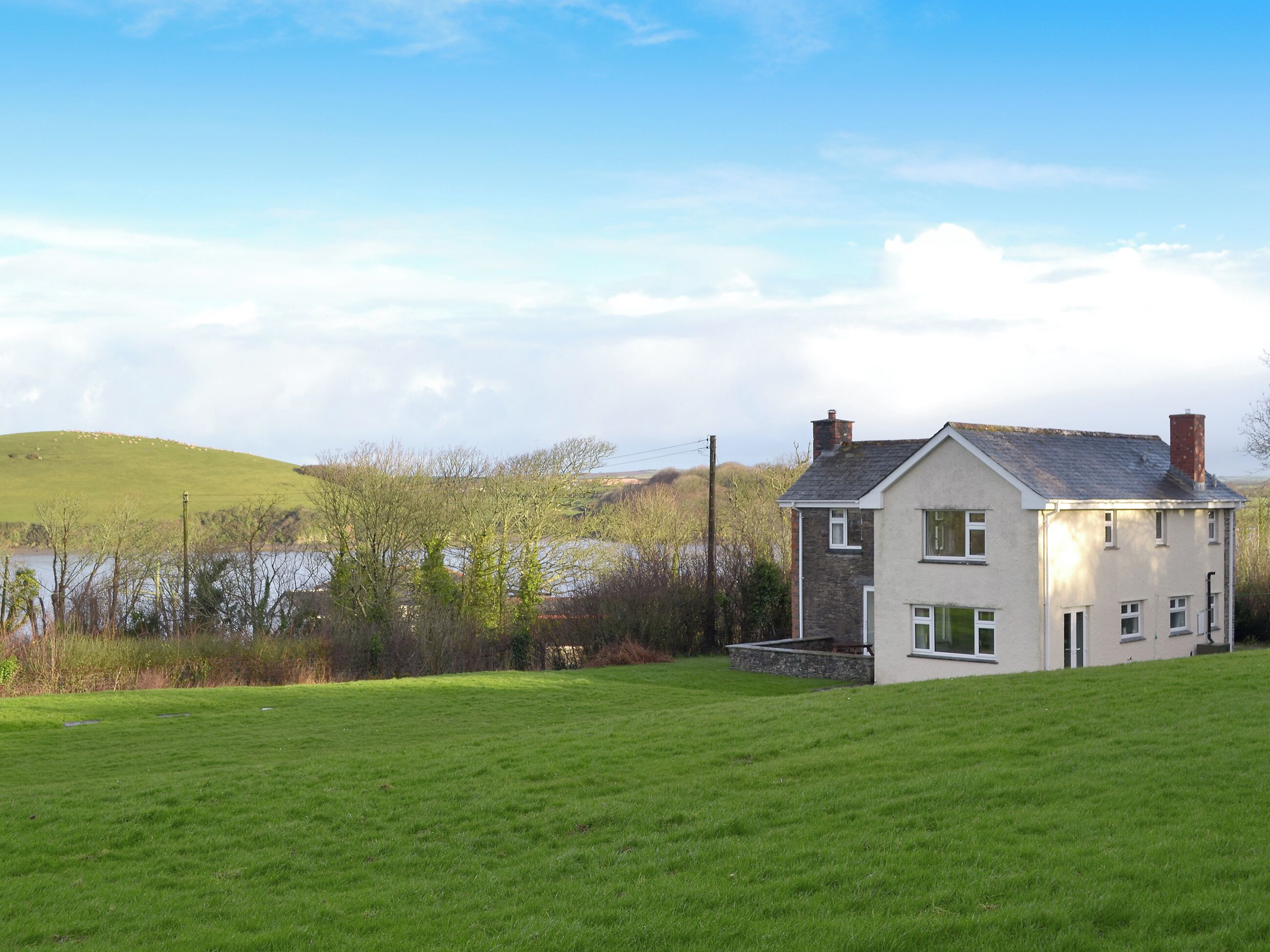 Une maison à deux étages avec une façade en pierre, une cheminée et une cour couverte d’herbe.