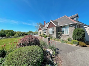 A two-story house with a stone facade, a red roof, and a well-maintained garden with red flowers and shrubs.