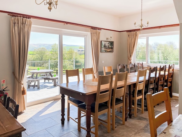 A dining area with a large table and chairs, a balcony with a view, and a chandelier.