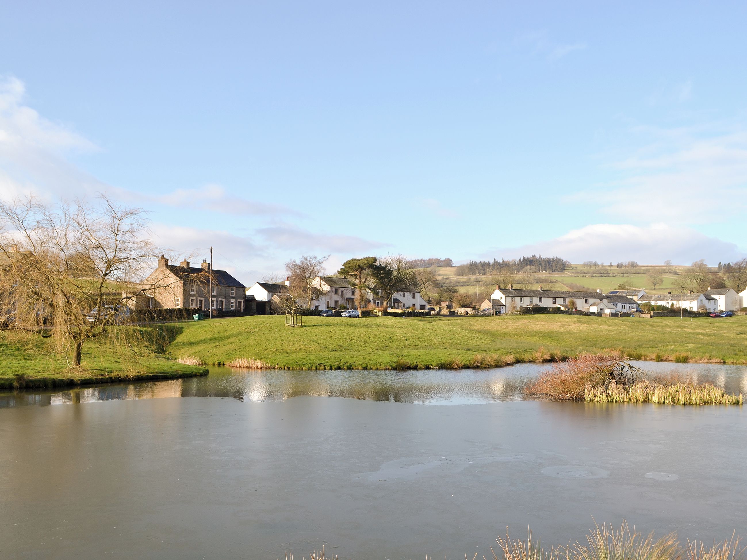 Un tranquilo pueblo junto al río, con casas y un estanque.