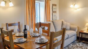 A dining area with a wooden table set for four, a bottle of wine, and wine glasses. There is a sofa and a small table with a lamp in the background. - 2 bedroom accommodation in Caldbeck, near Keswick (Caldbeck, near Keswick)