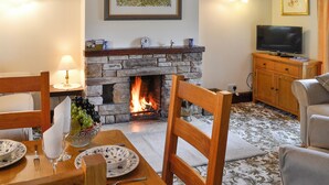 A cozy living room with a stone fireplace, wooden furniture, a television, and a framed picture on the wall. - 2 bedroom accommodation in Caldbeck, near Keswick (Caldbeck, near Keswick)