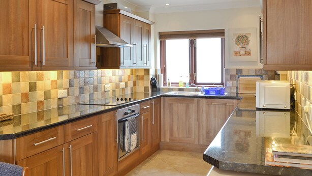 A modern kitchen with wooden cabinets, a black countertop, and a built-in oven. - 3 bedroom accommodation in Castletown (Castletown)