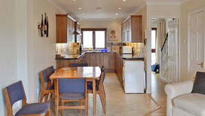 A modern kitchen with wooden cabinets, a dining area with a table and chairs, and a living room with a sofa. - 3 bedroom accommodation in Castletown (Castletown)
