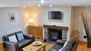 A living room with a fireplace, leather sofas, a coffee table, and a flat-screen TV. - 2 bedroom accommodation in Allonby, near Silloth (Allonby, near Silloth)
