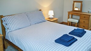 A neatly made bed with striped bedding, a bedside lamp, a wooden dresser with a mirror, and folded towels on the bed. - 2 bedroom accommodation in Allonby, near Silloth (Allonby, near Silloth)