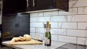 A kitchen with a marble backsplash, a cutting board with bread, a knife, and a bottle of champagne.