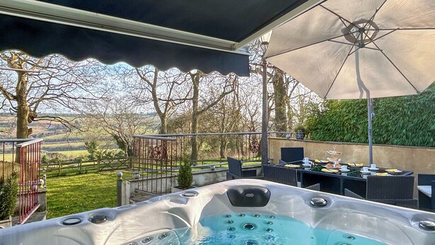 A hot tub with a view of a garden and a patio area with outdoor seating.