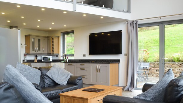 A modern living room with a leather sofa, a wooden coffee table, and a flat-screen TV mounted on the wall. - 6 bedroom accommodation in Wolsingham, near Stanhope (Wolsingham, near Stanhope)