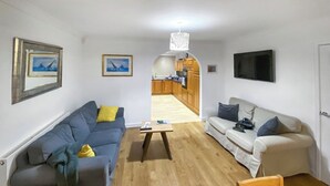A living room with a sofa, a coffee table, and a TV. There is a kitchen visible in the background. - 4 bedroom accommodation in Illogan, near Redruth (Illogan, near Redruth)