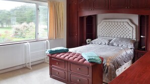 A bedroom with a large window, a bed with a headboard, a dresser with drawers, and a bedside table. - 4 bedroom accommodation in Illogan, near Redruth (Illogan, near Redruth)