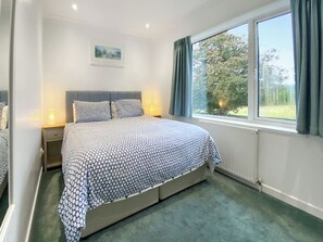 A bedroom with a bed, a nightstand, a window with curtains, a radiator, and a wall-mounted picture.