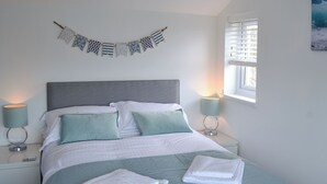 A neatly made bed with pillows, a bedside lamp, and a decorative banner on the wall. - 3 bedroom accommodation in Mevagissey (Mevagissey)