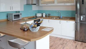 A modern kitchen with white cabinets, a stainless steel refrigerator, a microwave, and a sink with a faucet. - 3 bedroom accommodation in Mevagissey (Mevagissey)