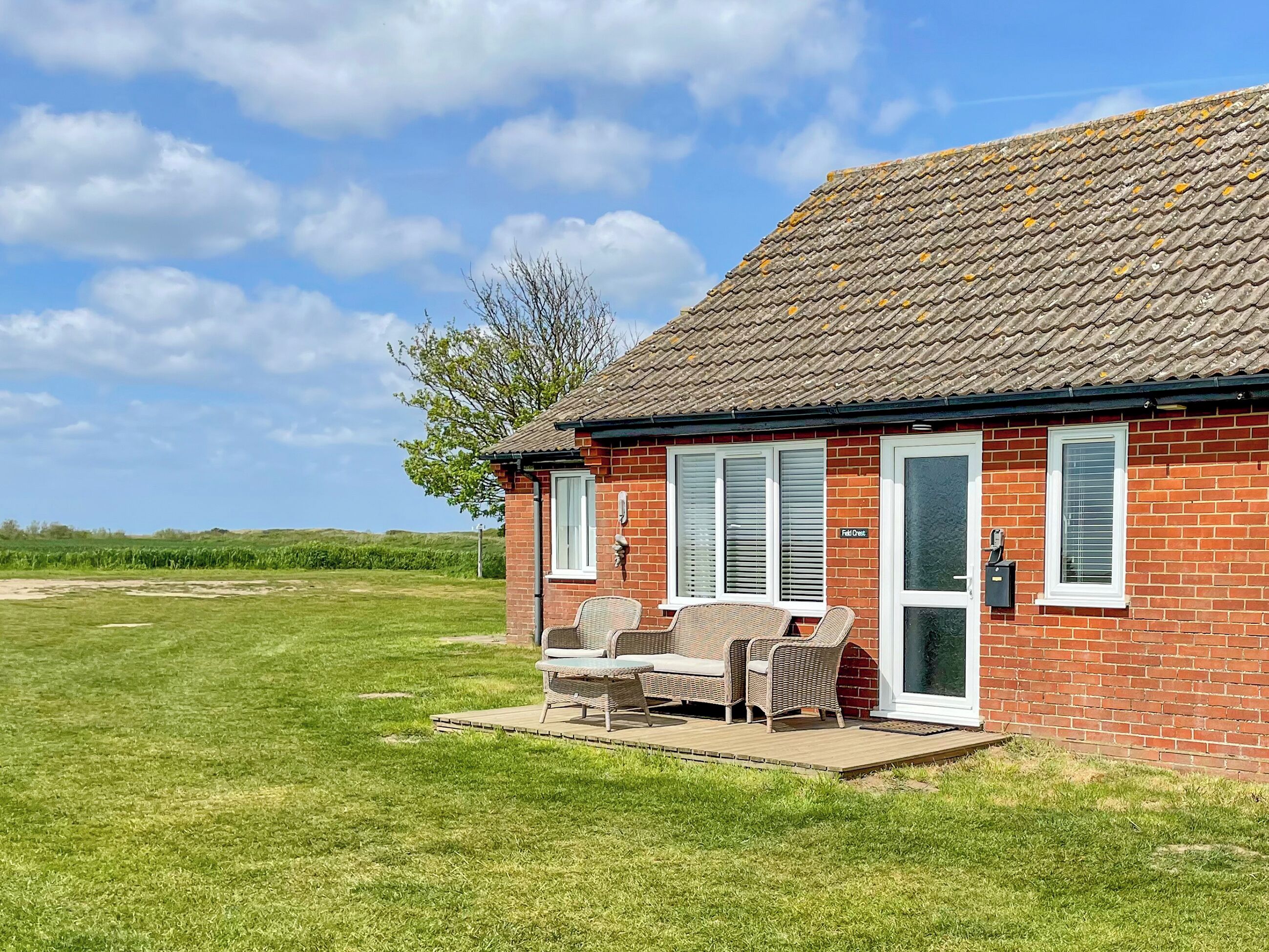 A brick house with a tiled roof, a patio with wicker furniture, and a grassy yard.