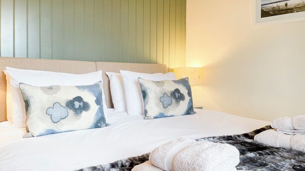 Habitación de hotel con cama, almohadas, una manta y un cuadro colgado en la pared.