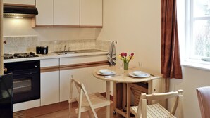 A compact kitchen with a stove, sink, and cabinets. There is a dining table with chairs and a small vase with flowers. - Jasmine Cottage - W41461 (Sturminster Newton)