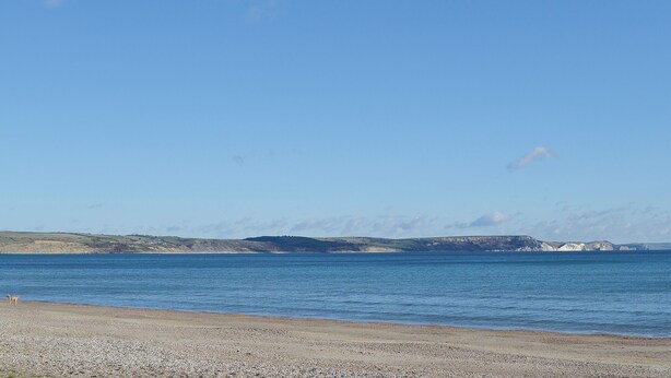 A beach with a pebbly shore, calm sea, and distant hills. - Jasmine Cottage - W41461 (Sturminster Newton)