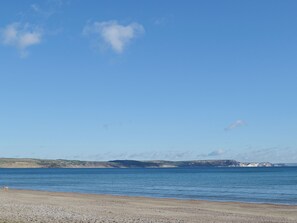 A beach with a pebbly shore, calm sea, and distant hills.