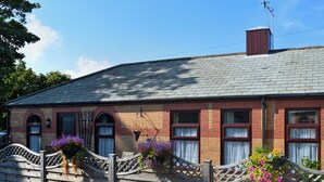 A brick building with a sloped roof, a wooden fence, and potted plants. - 4 Eldin Hall Cottages (Scarborough)