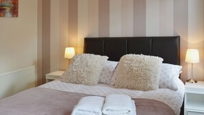 A neatly made bed with fluffy pillows, two bedside lamps, and folded towels on the bed. - 4 Eldin Hall Cottages (Scarborough)