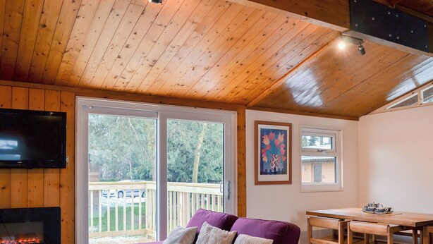 A cozy cabin interior with a wooden ceiling, a purple sofa, a TV, a fireplace, and a dining area with a table and chairs. - 2 bedroom accommodation in Charlcot, near Masham (Charlcot, near Masham)